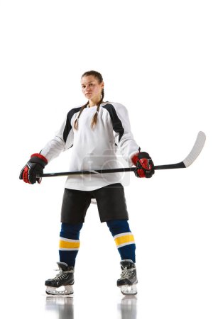 Téléchargez les photos : Jeune fille, joueuse de hockey en uniforme debout avec un bâton et posant isolée sur fond blanc. Champion. Concept de sport professionnel, compétition, jeu, action, passe-temps - en image libre de droit