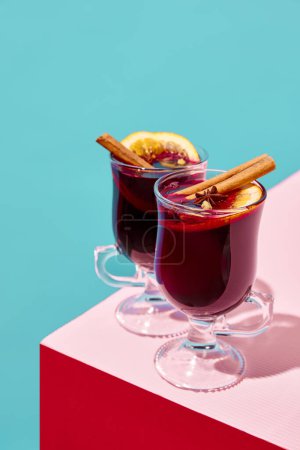 Téléchargez les photos : Verres avec délicieux vin chaud rouge aux oranges et à la cannelle sur fond coloré. Concept de saison d'hiver, vacances de Noël, boissons traditionnelles, goût. Affiche - en image libre de droit