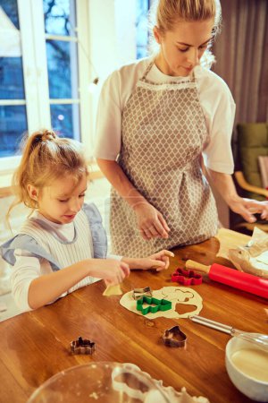 Photo for Woman, mother cooking Christmas cooking with her little daughter in modern kitchen in the evening. Following traditions. Concept of cookie day, motherhood, childhood, holidays, family - Royalty Free Image