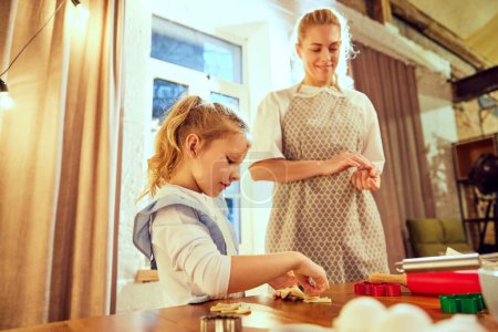 Photo for Beautiful, caring mother cooking with her little daughter at home in kitchen in evening. Teaching child to bake cookies. Winter season. Concept of cookie day, motherhood, childhood, holidays, family - Royalty Free Image