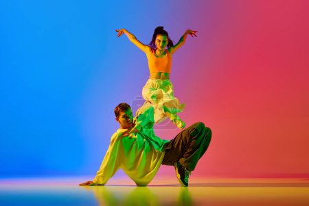 Photo for Talented, artistic, expressive young man and woman in modern clothes dancing hip hop against blue red background in neon. Concept of hobby, action, street style, contemporary dance, youth, fashion - Royalty Free Image