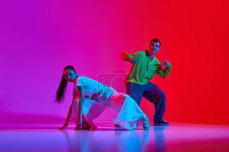Téléchargez les photos : Flux créatif. Jeune homme et femme en mouvement, dansant hip hop sur fond rouge rose au néon. Concept de hobby, action, street style, danse contemporaine, jeunesse, mode - en image libre de droit