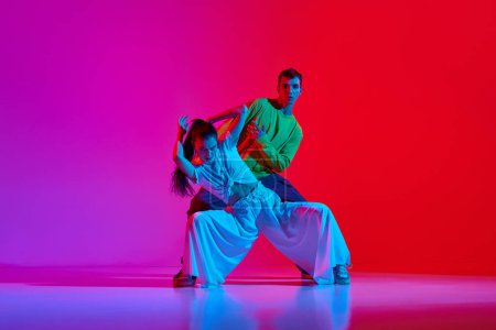 Photo for Freestyle performance. Young man and woman in motion, dancing hip hop against pink red background in neon light. Concept of hobby, action, street style, contemporary dance, youth, fashion - Royalty Free Image