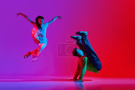 Téléchargez les photos : Une performance expressive. Jeune homme et femme, talentueux danseurs en mouvement, dansant hip hop sur fond rose rouge au néon. Concept de hobby, action, street style, danse contemporaine, jeunesse, mode - en image libre de droit
