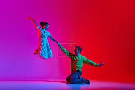 Photo for Expressive performance. Young man and woman, talented dancers in motion, dancing hip hop against pink red background in neon. Concept of hobby, action, street style, contemporary dance, youth, fashion - Royalty Free Image
