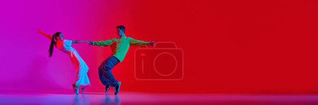 Photo for Young man and woman in notion, dancing hip hop against pink red background in neon light. Banner. Concept of hobby, action, street style, contemporary dance, youth, fashion - Royalty Free Image