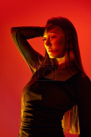Foto de Retrato de una joven chica hermosa posando sobre fondo de estudio naranja con reflexión de neón en la cara y el cuerpo. Concepto de arte, estilo moderno, cyberpunk, futurismo y creatividad - Imagen libre de derechos