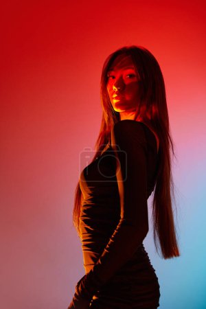Téléchargez les photos : Portrait de jeune belle fille posant sur fond studio orange avec réflexion néon sur le visage et le corps. Concept d'art, style moderne, cyberpunk, futurisme et créativité - en image libre de droit