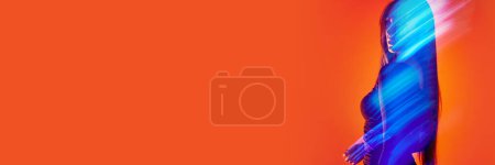 Téléchargez les photos : Portrait de jeune femme posant sur fond studio orange avec réflexion néon, lumières mélangées. Lumière fluorescente. Concept d'art, style moderne, cyberpunk, futurisme et créativité - en image libre de droit