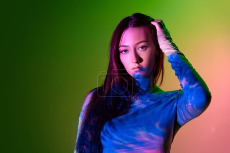 Téléchargez les photos : Portrait de jeune belle fille posant sur fond rose-vert dégradé avec réflexion néon. Art au néon abstrait. Concept d'art, style moderne, cyberpunk, futurisme et créativité - en image libre de droit