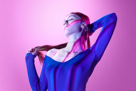 Téléchargez les photos : Belle, tendre jeune femme posant sur fond violet clair dans les néons avec des rayures néon réflexion. Concept d'art, style moderne, cyberpunk, futurisme et créativité, beauté - en image libre de droit