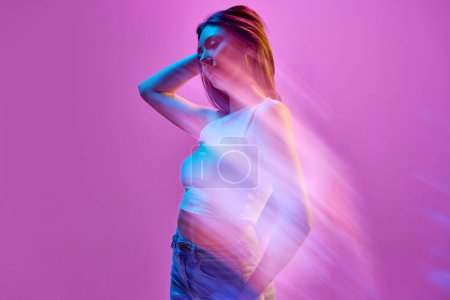 Foto de Retrato de mujer joven y elegante posando sobre fondo púrpura claro en luces de neón. Silueta. Reflejo de luces. Concepto de arte, estilo moderno, cyberpunk, futurismo y creatividad - Imagen libre de derechos