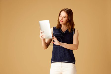 Foto de Mujer joven ins ropa elegante y gafas de sol de pie con la tableta contra fondo beige estudio. Negocios en línea, compras. Concepto de joven, emociones humanas, estilo de vida, moda, negocios - Imagen libre de derechos