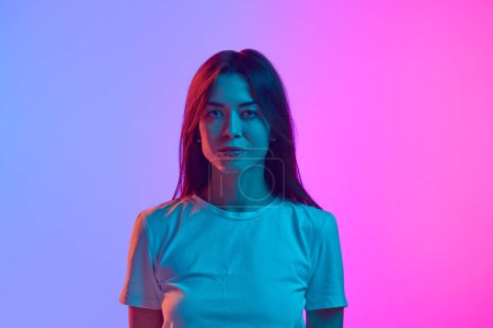 Photo for Portrait of young beautiful brunette woman looking at camera against gradient pink studio background in neon light. Concept of human emotions, lifestyle, youth culture, facial expression - Royalty Free Image