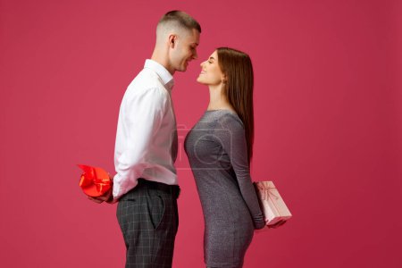 Photo for Beautiful young girl and man, couple holding presents behind back, standing against pink studio background. Concept of love, relationship, Valentines Day, emotions, lifestyle - Royalty Free Image