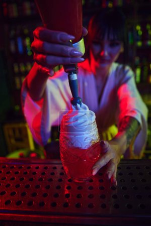 Photo for Beautiful young girl working as bartender in modern bar, making delicious cocktail, adding foam on top of sweet cocktail. Concept of occupation, nightlife, bar, party, alcohol drink, mixologist - Royalty Free Image