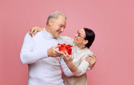 Photo for Happy, caring, loving senior couple, man and woman celebrating holiday, presenting gifts against pink studio background. Concept of marriage, relationship, Valentines Day, love, emotions, fashion - Royalty Free Image