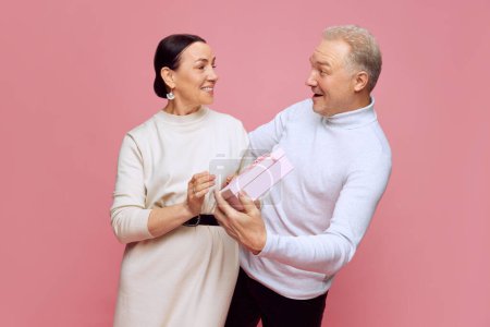 Photo for Loving and caring man, husband surprising his beautiful wife with present against pink studio background. Celebration. Concept of marriage, relationship, Valentines Day, love, emotions, fashion - Royalty Free Image