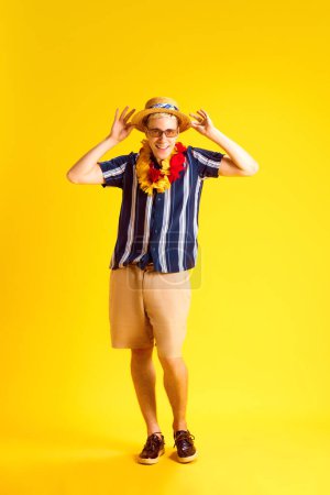 Photo for Smiling positive young man, tourist in casual clothes, sunglasses and straw hat posing against yellow studio background. Feeling happy. Concept of human emotions, youth, summer vacation, fashion - Royalty Free Image