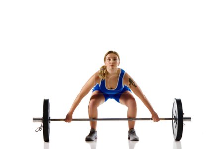 Photo for Athletic young girl with strong hands and body training, lifting heavy weight, barbell against white background. Concept of sport, strength, gym, healthy lifestyle, power and endurance, weightlifting. - Royalty Free Image