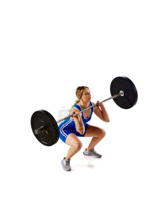 Photo for Concentrated strong young woman, athlete training doing squats, lifting heavy barbell against white background. Concept of sport, strength, gym, healthy lifestyle, power and endurance, weightlifting. - Royalty Free Image