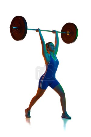 Photo for Full-length of young girl in blue bodysuit training, lifting heavy barbell against white background in neon light. Concept of sport, strength, gym, healthy lifestyle, power, endurance, weightlifting. - Royalty Free Image