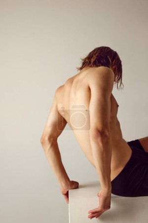 Photo for Young man with sportive, fit body sitting shirtless in underwear against grey studio background. Healthy back. Concept of mens beauty, health, body care, sportive lifestyle - Royalty Free Image