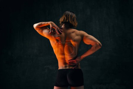 Photo for Healthy fit relief ack. Rear view of young shirtless man with muscular body standing in underwear against dark textured studio background. Concept of mens beauty, health, body art and aesthetics - Royalty Free Image