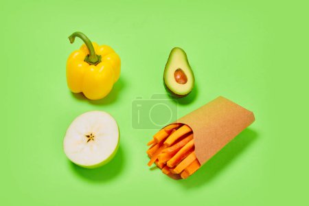 Photo for Carrots, avocado, yellow pepper and pear against green background. Healthy snacks. Concept of healthy food, nutrition, diet, organic products, diet and vegetable vitamins. Poster, ad - Royalty Free Image