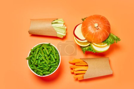 Photo for Healthy snacks. Green beans into popcorn basket, carrots, celery and vegetable burger against orange background. Concept of healthy food, nutrition, diet, organic products, diet, vitamins. Poster, ad - Royalty Free Image