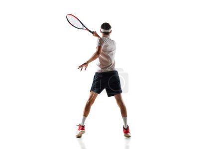 Téléchargez les photos : Vue arrière image du jeune homme en mouvement avec raquette, joueur de tennis pendant le match, l'entraînement isolé sur fond blanc. Concept de sport, passe-temps, mode de vie actif et sain, compétition - en image libre de droit