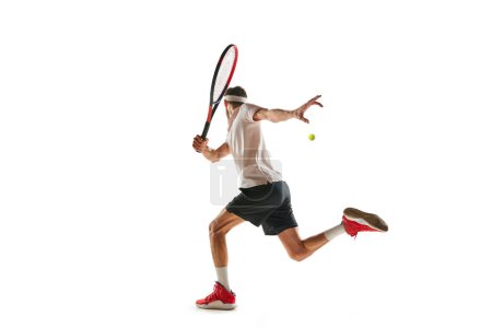 Téléchargez les photos : Sportif motivé, joueur de tennis pendant le match, en mouvement avec raquette, jouant isolé sur fond blanc. Concept de sport, passe-temps, mode de vie actif et sain, compétition - en image libre de droit