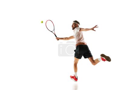 Téléchargez les photos : Homme compétitif, joueur de tennis pendant le jeu en mouvement, frapper la balle avec la raquette, jouer isolé sur fond blanc. Concept de sport, passe-temps, mode de vie actif et sain, compétition - en image libre de droit