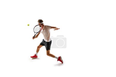 Téléchargez les photos : Homme concentré, athlète de tennis en mouvement pendant le joueur, pratiquant, jouant, frappant la balle avec raquette isolée sur fond blanc. Sport, passe-temps, mode de vie actif et sain, concept de compétition - en image libre de droit