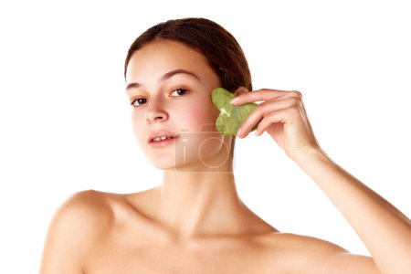 Photo for Beautiful young girl taking care after skin, using face massage tool gua sha against white background. Face lifting effect. Concept of natural female beauty, skin care, cosmetology and cosmetics - Royalty Free Image