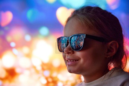 Photo for Happy smiling little girl, cheerful child in sunglasses looking on holiday celebration with fireworks. Reflection on glasses. Concept of Christmas, childhood, dreams, fantasy, happiness, inspiration - Royalty Free Image
