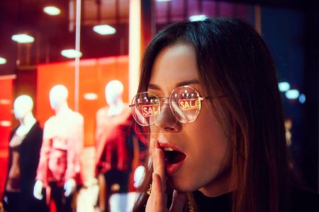 Photo for Happy and excited young woman looking on shop windows with neon lights reflection on glasses. Shopaholic, sales. Concept of human emotion, shopping, sales, holidays - Royalty Free Image