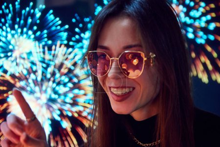 Photo for Beautiful young woman in sunglasses looking on fireworks. Lights reflection on eyewear. Holiday celebration. Concept of happiness, holidays, fun and joy, youth, emotions - Royalty Free Image