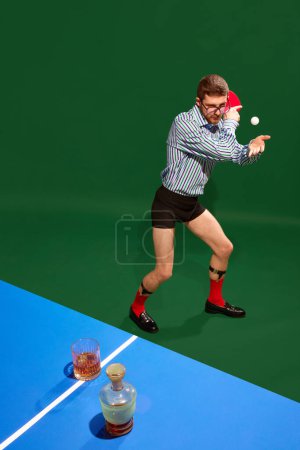 Photo for Top view. Funny creative photo with man un shirt and underweared playing table tennis with whiskey glass over green background. Concept of sport, leisure, hobby, creativity, fun and joy. Pop art - Royalty Free Image