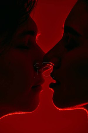 Foto de Rostros masculinos y femeninos, pareja joven besándose, mostrando amor sobre fondo rojo en luz de neón. Monocromo. Concepto de romance, amor, relación, pasión, juventud, citas, felicidad - Imagen libre de derechos