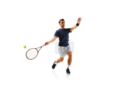 Téléchargez les photos : Jeune homme athlétique, joueur de tennis en mouvement, frappant balle avec raquette isolée sur fond blanc. Jeu dynamique. Concept de sport professionnel, compétition, jeu, mathématiques, passe-temps, action - en image libre de droit