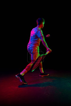 Foto de Joven, jugador de tenis durante el juego, jugando, practicando sobre fondo oscuro en luz de neón. Concepto de deporte profesional, competición, juego, matemáticas, hobby, acción - Imagen libre de derechos