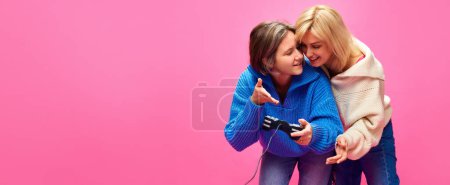 Photo for Beautiful young women, lesbian couple playing play station, video games together over pink studio background. Concept of lgbt community, love, Valentines day, freedom, acceptance, February 14th - Royalty Free Image