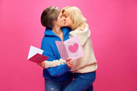 Photo for Happy young women, lesbian couple celebrating romantic holiday, kissing over pink studio background. Concept of lgbt community, love, Valentines day, freedom, acceptance, February 14th - Royalty Free Image