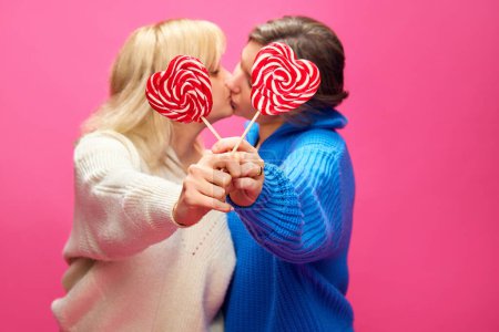 Photo for Young women, lesbian couple in casual clothes kissing behind candies over pink studio background. Concept of lgbt community, love, Valentines day, freedom, acceptance, February 14th - Royalty Free Image