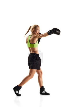Téléchargez les photos : Un coup de poing. Jeune femme sportive au corps musclé pratiquant la boxe isolée sur fond blanc. Concept de sport, mode de vie actif et sain, force et endurance, soins corporels - en image libre de droit