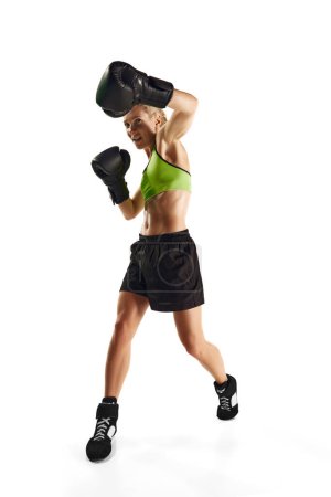 Téléchargez les photos : Jeune femme musclée et concentrée, entraînement d'athlète de boxe, coups isolés sur fond blanc. Concept de sport, mode de vie actif et sain, force et endurance, soins corporels - en image libre de droit