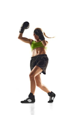 Téléchargez les photos : Jeune femme musclée, athlète de boxe pratiquant, frappant, s'entraînant isolé sur fond blanc. Concept de sport, mode de vie actif et sain, force et endurance, soins corporels - en image libre de droit