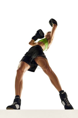 Téléchargez les photos : Vue du bas de la jeune femme musclée, athlète de boxe en mouvement, entraînement, coups isolés sur fond blanc. Concept de sport, mode de vie actif et sain, force et endurance, soins corporels - en image libre de droit