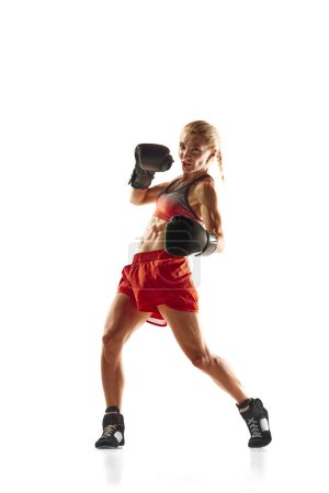 Téléchargez les photos : Vue du bas de la jeune femme musclée, athlète de boxe en mouvement, entraînement, coups isolés sur fond blanc. Concept de sport, mode de vie actif et sain, force et endurance, soins corporels - en image libre de droit